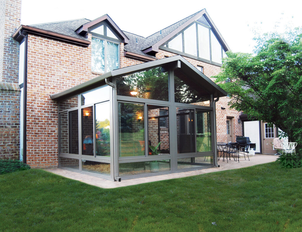 Custom Deck Builder for Homeowners - M2 Decks & Enclosures Exterior view of a 3-season sunroom featuring a gabled roof and large glass panels attached to a brick residential home.
