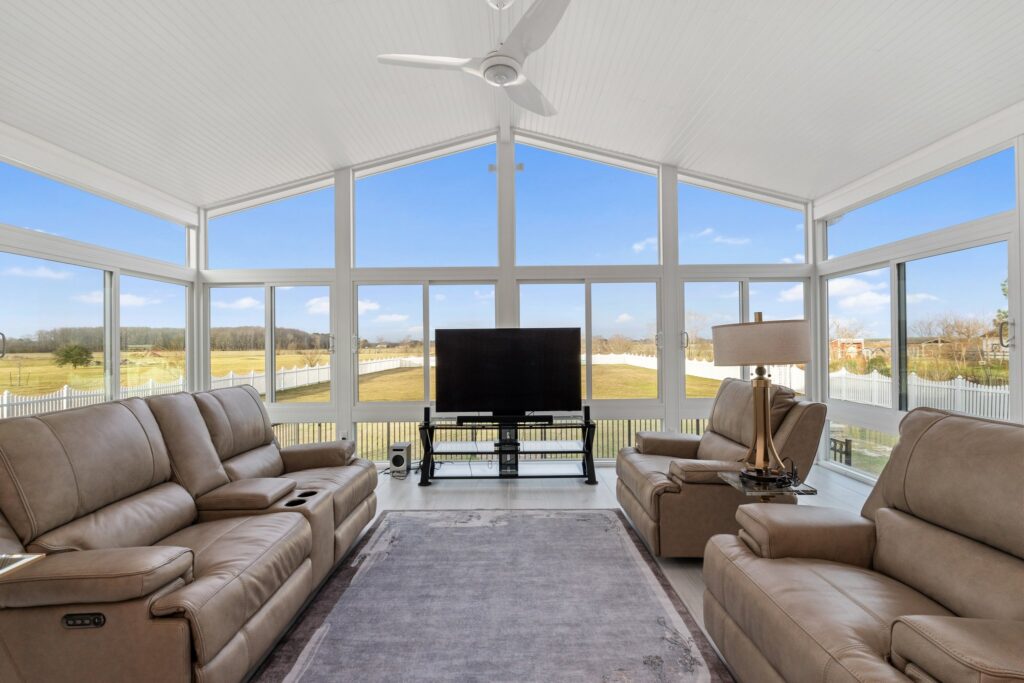 Interior of a spacious 4-season sunroom featuring large windows, vaulted ceilings with a fan, and a full living room set with a TV.