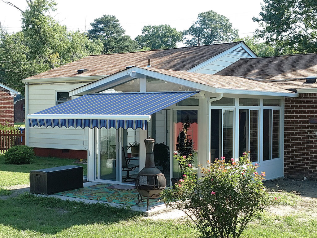 A blue and white striped Model 2 retractable awning installed over the sliding glass door of a white 3-season sunroom.