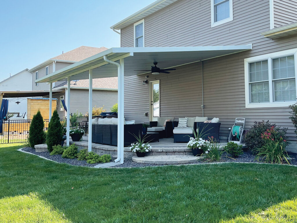Custom Deck Builder for Homeowners - M2 Decks & Enclosures A white aluminum patio cover with an integrated ceiling fan installed over an elevated stone paver patio with outdoor lounge seating.