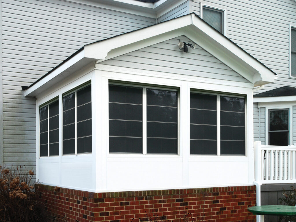 Exterior of a white gabled sunroom with 4-track stacking windows and a brick base, illustrating a 3-season conversion from a standard screen room.