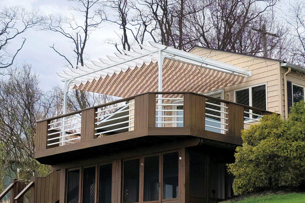 A white aluminum pergola with a retractable striped canopy installed on an elevated brown wood deck, demonstrating the durability of aluminum in the Wisconsin climate.