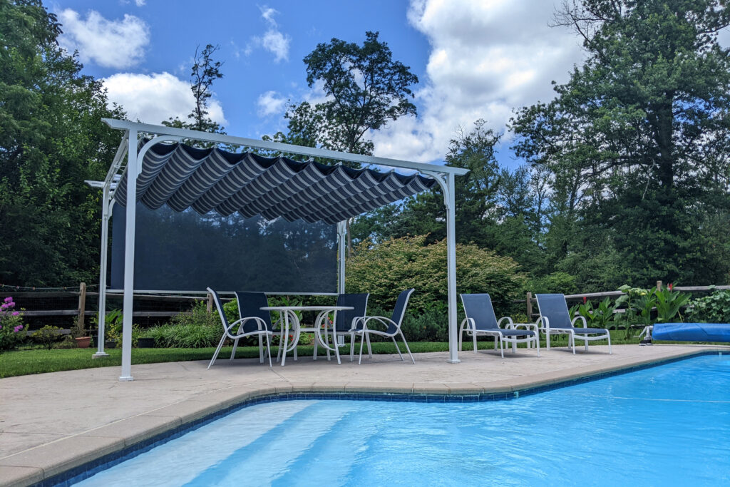 A white poolside pergola with a striped retractable fabric canopy and a motorized privacy screen, featuring an outdoor dining set next to a swimming pool.