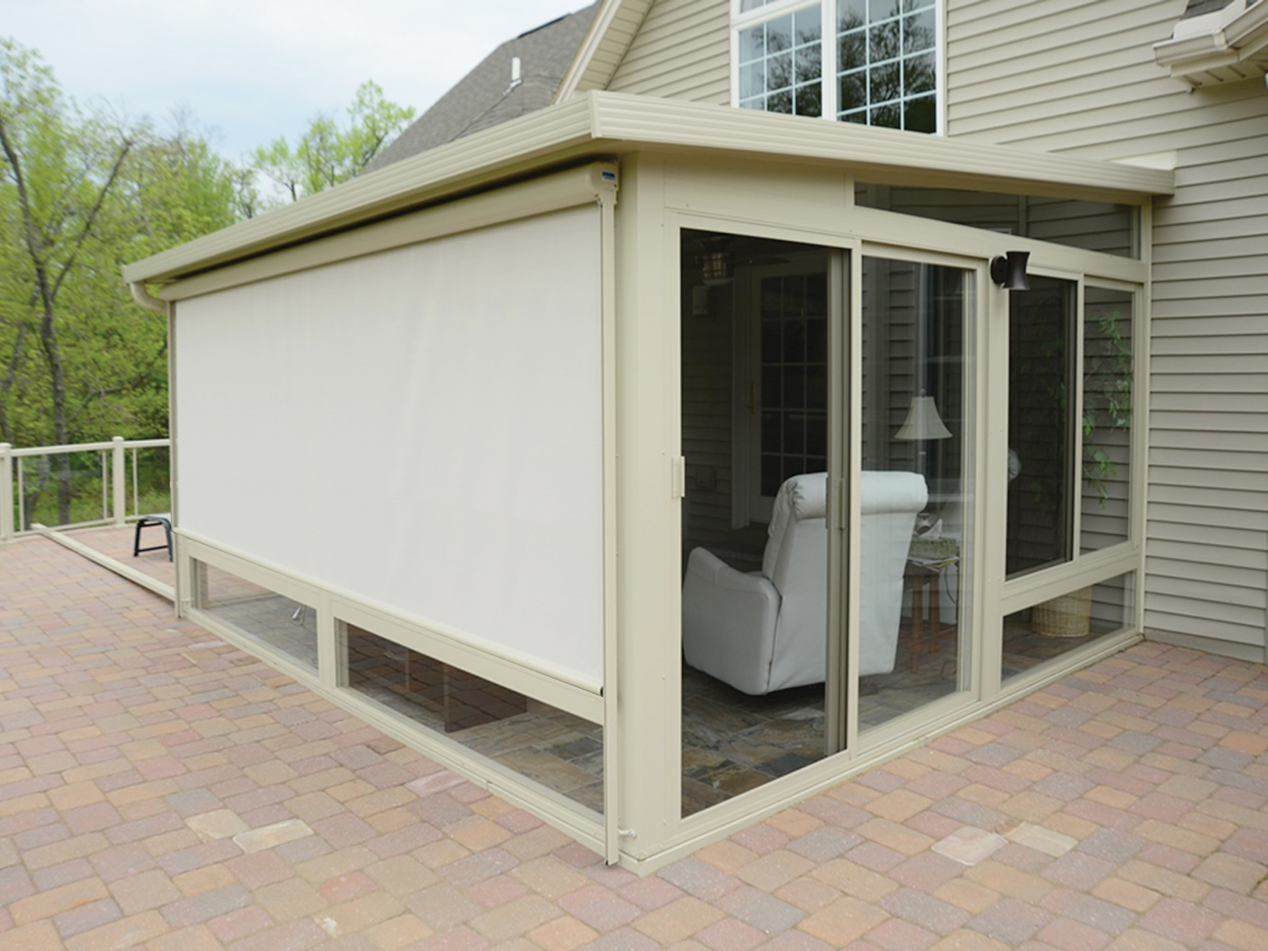 Best Deck Company - M2 Decks and Enclosures Exterior of a tan sunroom with a large retractable shade lowered over glass walls, built on a custom paver patio in a Wisconsin backyard.