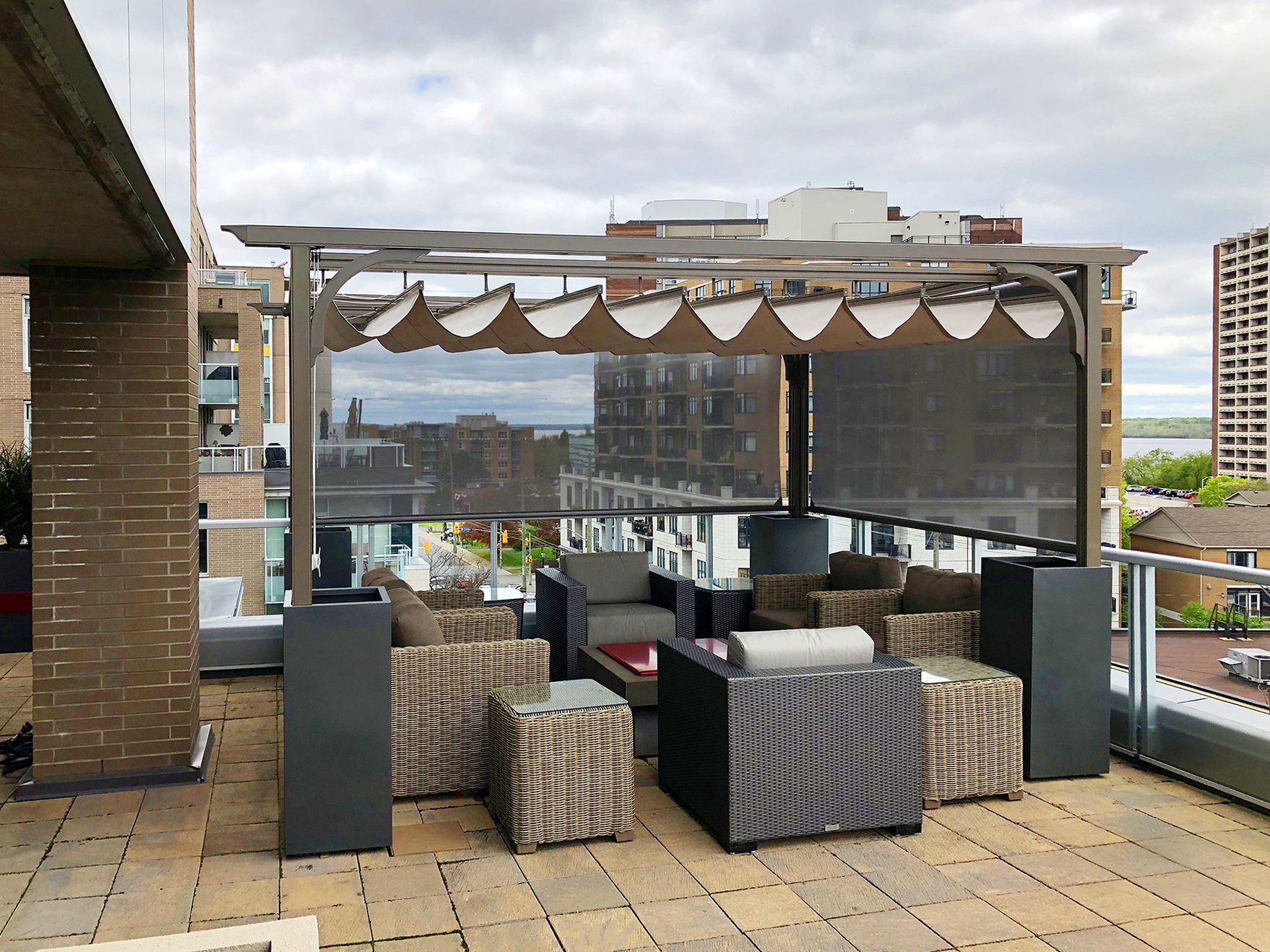Best Deck Company - M2 Decks and Enclosures A modern grey aluminum canopy with a tan retractable roof and dark mesh side screens on a high-end urban rooftop patio.
