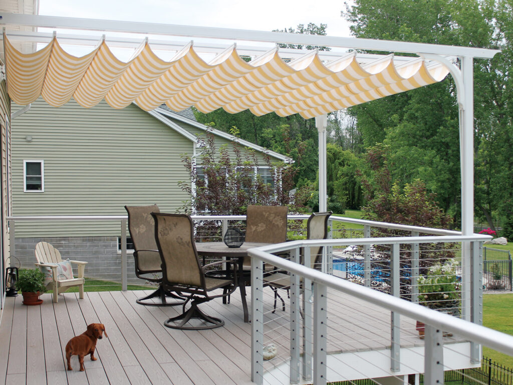 Exterior of an elevated deck with a white aluminum canopy frame and a yellow and white striped retractable fabric cover.