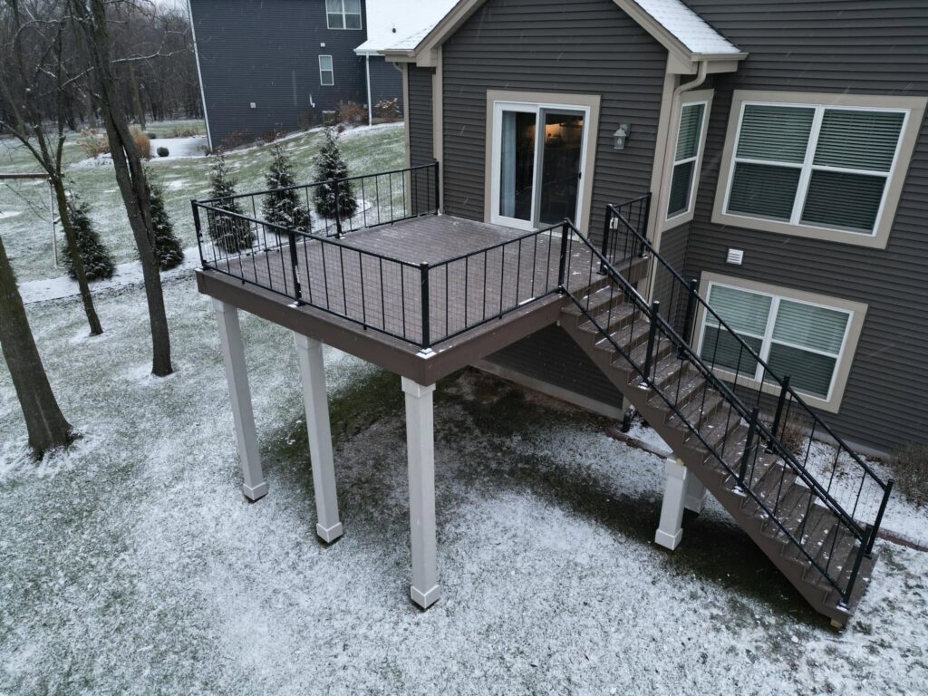 Elevated second-story composite deck with black metal railing sitting under light snow cover on a home in Wisconsin.