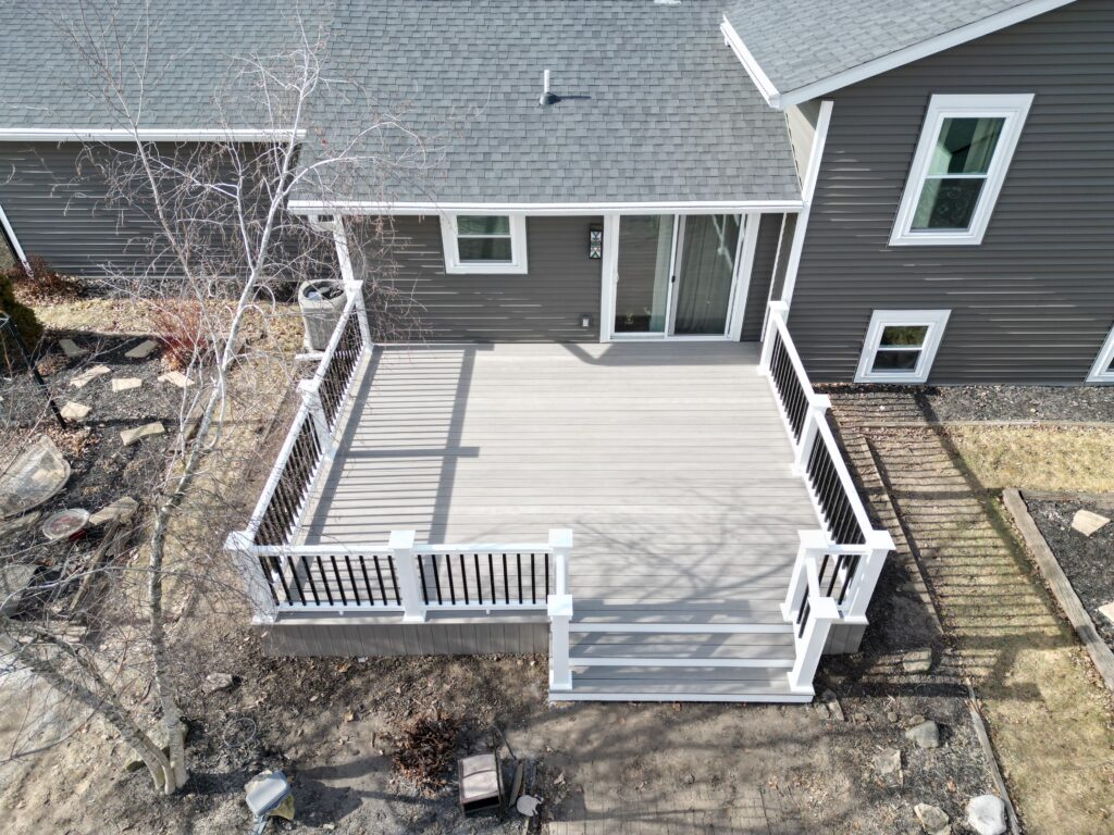 Overhead drone shot of a custom grey TimberTech composite deck with white and black railings installed on a dark siding home in Wisconsin.